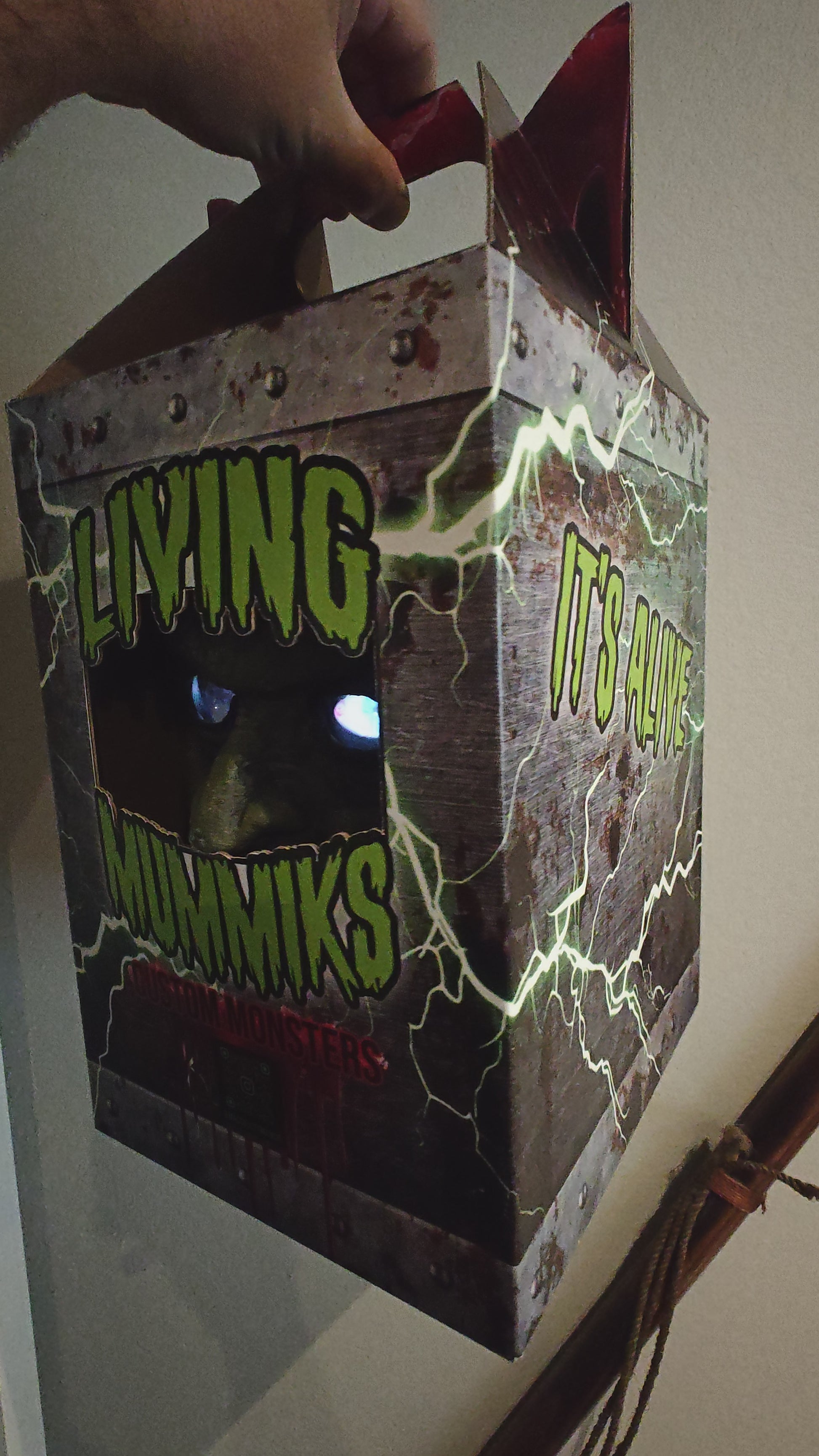 Living Mummiks custom monsters packaging with a hand holding the box.
Frankenstein  Monster 3D printed  Bust with Living Mummiks Display Box  and Digital eyes kit installed. Halloween, Horror Display.